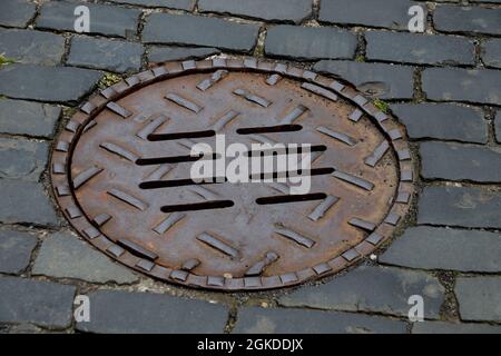 Metallschachtabdeckung auf einer alten gepflasterten Dorfstraße Stockfoto