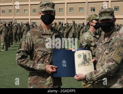 Army Reserve Col. Garrett Kolo, 33. Sustainment Command (Expeditionary), hält seine norwegische Fußmarschurkunde, die ihm von Army Reserve Brig überreicht wurde. General Justin Swanson, der kommandierende General des 21. ESC, bei der Anerkennungszeremonie am 2021. März im Camp Arifjan, Kuwait. Kolo, war der Top-Finisher im NFM, als er die Ziellinie überquerte und den 18.6-Meilen-Kurs mit einem 25-Pfund-Ruck in 2 Stunden und 52 Minuten absolvierte. Stockfoto