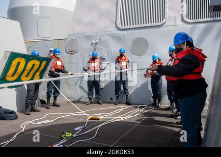 PAZIFISCHER OZEAN (22. März 2021) – Seeleute, die dem amphibischen Transportdock der San Antonio-Klasse USS Portland (LPD 27) zugewiesen wurden, neigen während einer Auffüllung auf See mit dem Trockenfrachtschiff USNS Richard E. Byrd der Lewis- und Clark-Klasse (T-AKE 4) die Telefon- und Entfernungslinie. Portland führt derzeit Routineoperationen in der dritten US-Flotte durch. Stockfoto