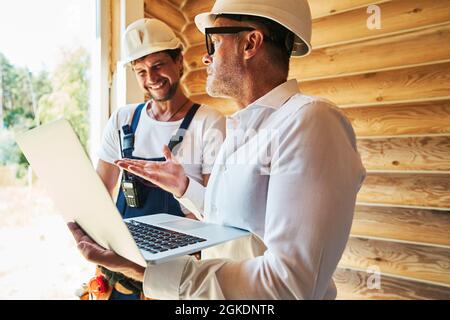 Bauingenieur mit Laptop, der dem Hausbauer etwas erklärt Stockfoto