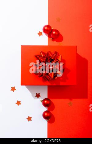 Komposition aus rotem weihnachtsgeschenk mit Kugeln auf weißem und rotem Hintergrund Stockfoto