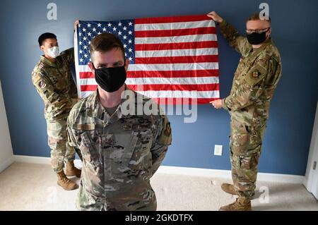 Senior Airman Cedric Fajardo der US Air Force (links) und Staff Sgt. Thomas Hill (rechts), 1st Combat Camera Squadron (CTCS), Cyber Systems Technicians, von der Joint Base Charleston, South Carolina, nimmt an einer Neuzuteilungszeremonie für Staff Sgt Teil. David Rhoton (vorne), 1. CTCS, Client Systems Supervisor, in seinem Haus in Summerville, South Carolina, 24. März 2021. Diese einzigartige Zeremonie fand während eines Videotreffens des Roundtable der Survivor Advocacy der Luftwaffe statt und wurde vom Stabschef der Luftwaffe, General Charles Q. Brown, offiziell abgehalten. Stockfoto