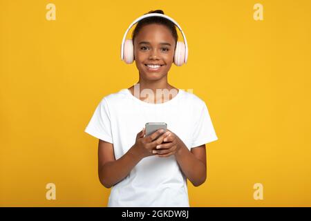 Frohes, schwarzes Mädchen, Schülerin in weißem T-Shirt und kabellosen Kopfhörern, hört Unterricht, lernt Sprache Stockfoto