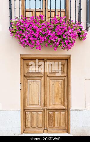 Schöne hölzerne Eingangstür zu einem Haus mit einem Balkon voller Fuchsia Blumen Stockfoto