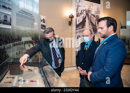 Roderick Gainer (links), Historiker, Nationalfriedhof von Arlington; Führung durch das Memorial Amphitheatre Ausstellungsraum für die Medal of Honor-Empfänger der US Army 1st LT. Brain Thacker (Mitte) und den U.S. Navy Master Chief Special Warfare Operator Edward Byers, Jr. (rechts) im Memorial Amphitheatre Ausstellungsraum auf dem Arlingotn National Cemetery, Arlington, Virginia, 25. März 2021. Thacker und Byers nahmen an einer Ehrenfestung der Armee im Grab des Unbekannten zu Ehren des Ehrenmedaillentages Teil. Stockfoto