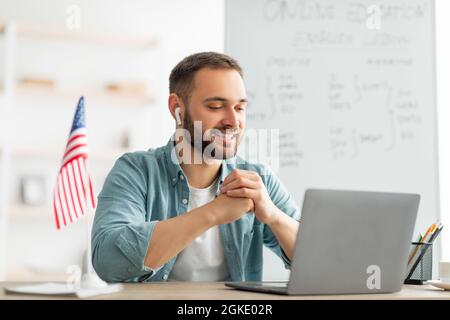 Glücklicher männlicher Lehrer, der Englischunterricht im Internet mit einem Laptop im Heimbüro gibt. Modernes Fernschulungskonzept Stockfoto