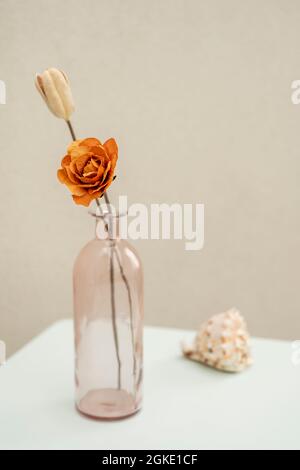 Rosa Vase Flasche mit oranger Rose auf pastellblauem Tisch und Muschelschale im Hintergrund Stockfoto