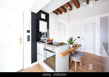 Kleine graue Insel mit Cerankochfeld und Eichen-Bürotisch mit Hockern und Frühstück mit Früchten in der Ferienwohnung Stockfoto