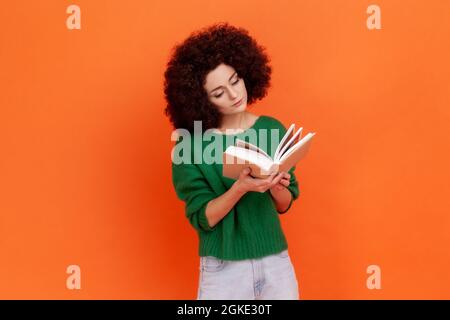 Attraktive konzentrierte Frau mit Afro-Frisur trägt grünen lässigen Stil Pullover Lesen Interessantes Buch, sehr aufmerksam. Studio-Sho Stockfoto