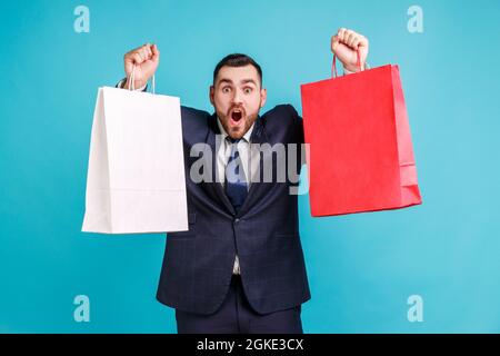 Aufgeregter Mann im offiziellen Stil Anzug, Raising Taschen und Geschrei aus dem Glück, begeistert von Einkaufen im Modegeschäft begeistert, Sparsamkeit Verkauf. Innen s Stockfoto