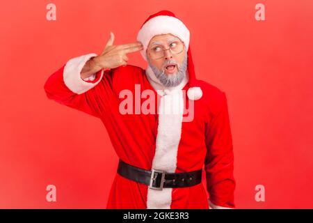 Tötet mich bitte! Älterer Mann mit grauem Bart, trägt das weihnachtsmann-Kostüm und zielt mit verzweifeltem Ausdruck mit der Fingerwaffe auf den Kopf, mit Selbstmordgesten. Innen s Stockfoto