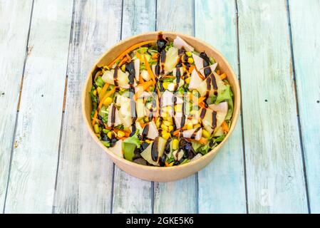 Hawaiianischer Salat mit Gemüse, Ananas, Käse und Schinken in einer Pappschale zur Hauszustellung auf Holztischen Stockfoto