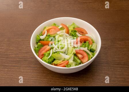 Gartensalat mit gehackten Tomaten, Salat und knuspriger weißer Zwiebel in einer einfachen weißen Schüssel und einem Holztisch Stockfoto