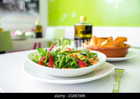 Grüner Rucola-Salat, gehackte Erdbeeren, Walnüsse und Parmesankäse in Flocken, Olivenöl und Essig-Vinaigrette Stockfoto