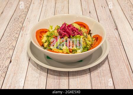 Riesige Salatschüssel mit Avocado und süßem Mais, roten Zwiebeln, geschnittenen Tomaten, Escarole und Sesam und Mohn Stockfoto