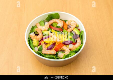 Nach Hause liefern Schüssel mit einem Salat aus grünem Spinat, gelben Mais, rosa gekochte Garnelen, rohe rote Paprika und gewürfelte rote Zwiebel Stockfoto