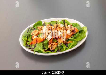 Weißes Tablett mit Spinatsalat mit gerösteten roten Paprika, Walnüssen, frischem Käse und Balsamico aus Modena Stockfoto