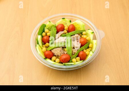 Salat in einer transparenten Kunststoffschüssel zur Hauszustellung mit gebratener Avocado, gekochten Kichererbsen, roher Gurke, Bonito aus der Dose, Kirschtomaten und Spinat Stockfoto