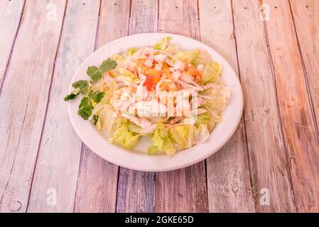 Chinesischer Salat mit Garnelen, Surimi, Eisbergsalat, geriebener Karotte und frischer Petersilie auf einem Holztisch Stockfoto