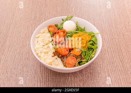 Gartensalat mit Rucola-Sprossen, geschälten Kirschtomaten, Kokosnuss, Reis und Kürbiscreme auf einer weißen Schüssel. Stockfoto