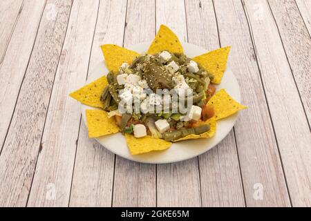 Toller mexikanischer Nopalesalat mit Käse, Tomaten, Salat, gehacktem Frischkäse und gelben Mais-Chips auf weißem Tisch Stockfoto