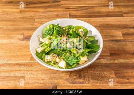 Spinatsalat mit gehackten Birnen, Menge Pinienkerne und Blauschimmelkäse in einer weißen Schüssel Stockfoto