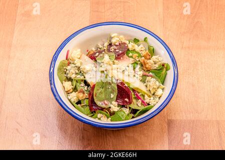Spinatsalat mit Rote-Beete-Scheiben, dünnen Birnenscheiben, zerbröseltem Blauschimmelkäse, Nüssen in einer emaillierten Metallschüssel Stockfoto