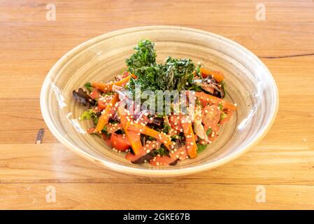 Köstlicher und gesunder Salat aus verschiedenen Gemüsesorten und Grünkohl in einer schönen beigefarbenen Porzellanschüssel auf einem Holztisch Stockfoto