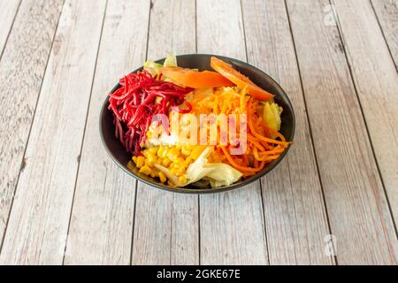 Gemüsesalat mit süßem Mais, Karotten und roter Rübenschale, gewürfelten Tomaten und Eisbergsalat in einer schwarzen Schüssel Stockfoto