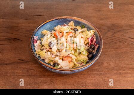 Griechischer Salat mit Joghurt, Samen, schwarzen Oliven, Salat und gehackten Tomaten auf einer blauen Schüssel Stockfoto