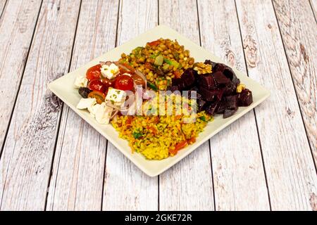 Verkostung griechischer mediterraner Salate mit Linsen, Bulgur, gewürfelten Rüben, Feta-Käse und Kirschtomaten auf einem quadratischen Teller Stockfoto