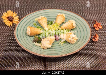 Blätterteigkegel, gefüllt mit russischem Salat mit Mayonnaise und gekochter Kartoffel auf einem grünen Teller auf einer braunen Tischdecke Stockfoto