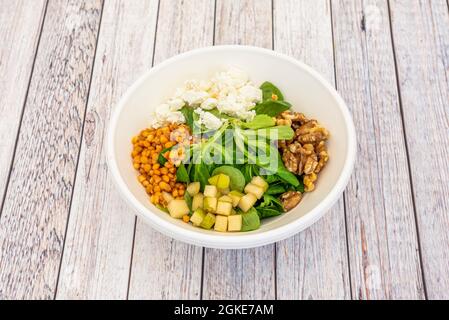 Geschmorter Linsensalat mit zerbröseltem Frischkäse, Lammsalat und Spinatsprossen, Apfelquadraten und gehackten kalifornischen Walnüssen Stockfoto