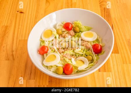 Weiße Schüssel mit gemischtem Thunfischkonservensalat mit gekochtem Ei, Kirschtomaten, Eisbergsalat und spanischen entsteinten Oliven Stockfoto