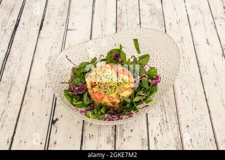 Quinoa-Salat mit Tomaten und Avocado-Tartare, Bohnensprossen, Streifen grünem Spinat und purpurem Grünkohl auf einer schönen Glasschüssel Stockfoto