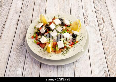 Türkischer Salat mit gewürfeltem Feta-Käse, gehackten schwarzen Oliven, gehacktem Gurken und Paprika, Limettendressing auf weißem Teller Stockfoto