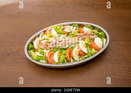 Metallsalatschale zum Teilen mit viel Eisbergsalat, Tomaten und gehacktem gekochtem Ei, Scheiben weißer Zwiebel und Thunfisch in der Dose. Stockfoto