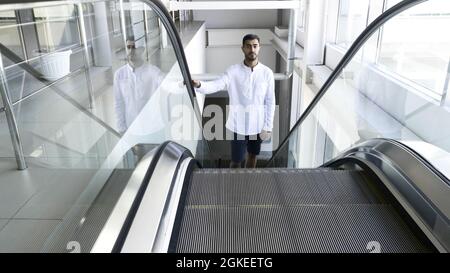 Mann in einem weißen Hemd, der die Rolltreppe im Business Center hochfährt. HDR. Junger Mann auf der Rolltreppe im Kaufhaus Stockfoto