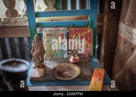 Gebetsbilder mit Hindu-Göttinnen, kleiner Götterstatue, Räucherstäbchen und Räucherbrennern auf einem Stuhl, Hausaltar in der Hütte eines Fischers Stockfoto