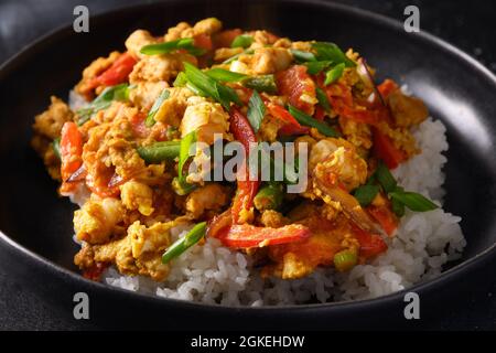 Thailändisches Frühstück Gai Pad Pongali mit Huhn, Eiern, würziger, gelber thai-Paprikapaste, Tomaten, Reis in schwarzer Schüssel im Wok. Nahaufnahme. Panasiatische Küche. Stockfoto