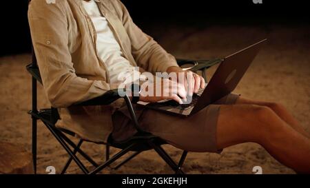 Körper eines Mannes, der einen Laptop auf einem Campingstuhl benutzt Stockfoto