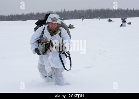 Army Staff Sgt. Zach Hurley, ein Fallschirmjäger mit Hauptquartier und Hauptquartier, 1. Bataillon, 501. Fallschirmjäger-Infanterie-Regiment, 4. Infanterie-Brigade-Kampfteam (Airborne), 25. Infanterie-Division, U.S. Army Alaska, Wandern Sie durch den Schnee, während Sie während eines simulierten Fallschirmsprungangriffs in der Malemute Drop Zone auf der Joint Base Elmendorf-Richardson, Alaska, zum Rallyepunkt weiterfahren, 2021. März 31. Die Soldaten sind Teil der einzigen pazifischen Luftbrigade der Armee, die in der Lage ist, sich schnell weltweit zu entsenden, und werden für militärische Operationen unter strengen Bedingungen geschult. Stockfoto