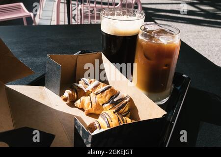 Zwei Gläser Cold Brew Coffee, einer davon mit Nitro und der andere mit Milch, und ein Tablett mit Schokoladencroissants Stockfoto