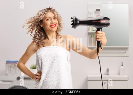 Junge Frau mit einem lockigen Haar, das in einem Handtuch mit einem Haardiffusor im Badezimmer eingewickelt ist Stockfoto