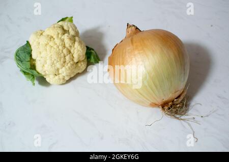 Eine riesige Zwiebel und/oder ein winziger Blumenkohl auf Marmoroberfläche - ein oder beide Gemüse ist ungewöhnlich klein oder unerwartet groß. Zwiebel ist größer als Cauli. Stockfoto