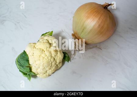 Eine riesige Zwiebel und/oder ein winziger Blumenkohl auf Marmoroberfläche - ein oder beide Gemüse ist ungewöhnlich klein oder unerwartet groß. Zwiebel ist größer als Cauli. Stockfoto