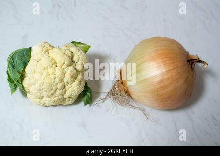 Eine riesige Zwiebel und/oder ein winziger Blumenkohl auf Marmoroberfläche - ein oder beide Gemüse ist ungewöhnlich klein oder unerwartet groß. Zwiebel ist größer als Cauli. Stockfoto