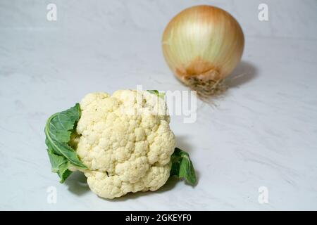 Eine riesige Zwiebel und/oder ein winziger Blumenkohl auf Marmoroberfläche - ein oder beide Gemüse ist ungewöhnlich klein oder unerwartet groß. Zwiebel ist größer als Cauli. Stockfoto