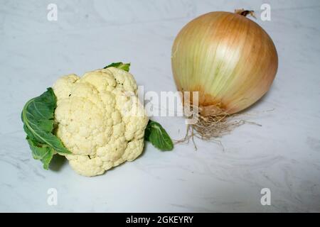 Eine riesige Zwiebel und/oder ein winziger Blumenkohl auf Marmoroberfläche - ein oder beide Gemüse ist ungewöhnlich klein oder unerwartet groß. Zwiebel ist größer als Cauli. Stockfoto