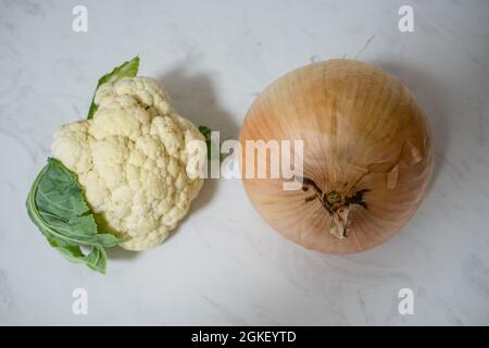 Eine riesige Zwiebel und/oder ein winziger Blumenkohl auf Marmoroberfläche - ein oder beide Gemüse ist ungewöhnlich klein oder unerwartet groß. Zwiebel ist größer als Cauli. Stockfoto